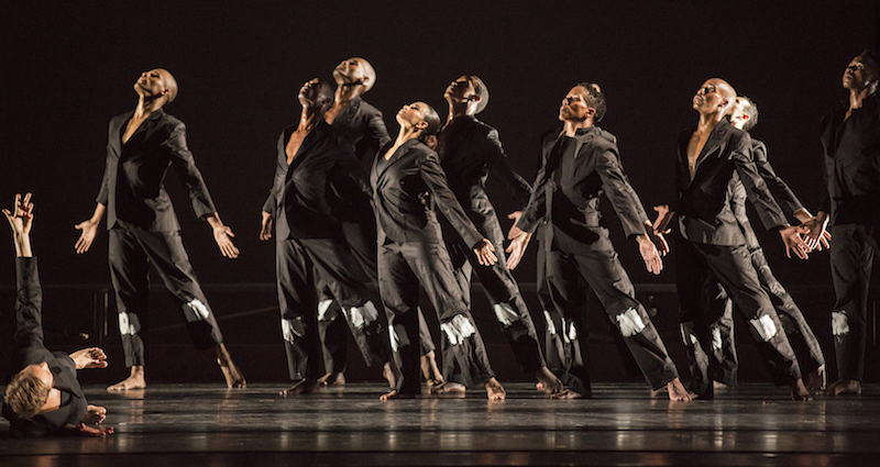 Ailey dancers dress in black suits  have their palms open and heads tilted to the ceiling